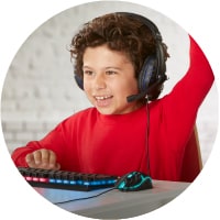 A smiling child at her computer wearing headphones and raising her hand